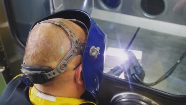 Bald worker connects metal parts by welding in closed box — Stock Video