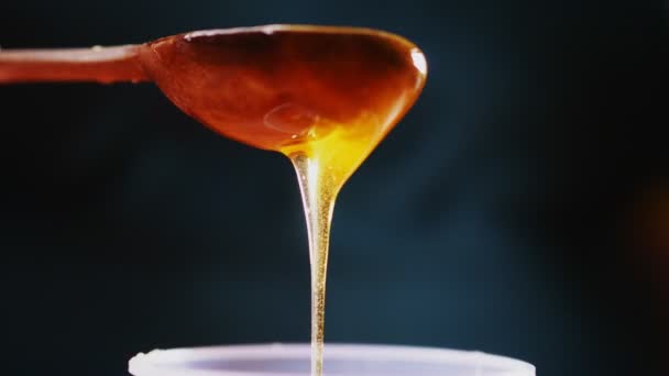 Persoon schenkt smakelijke honing van lepel op donkere achtergrond — Stockvideo