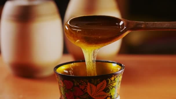 Cuillère en bois avec verser du miel sur un bol décoré gros plan — Video