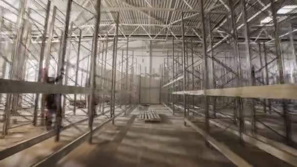 Рабочие собирают металлические стеллажи на просторном складе завода — стоковое видео