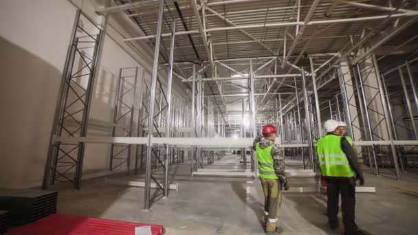 Рабочие собирают металлические стеллажи в светлых просторных складах — стоковое видео