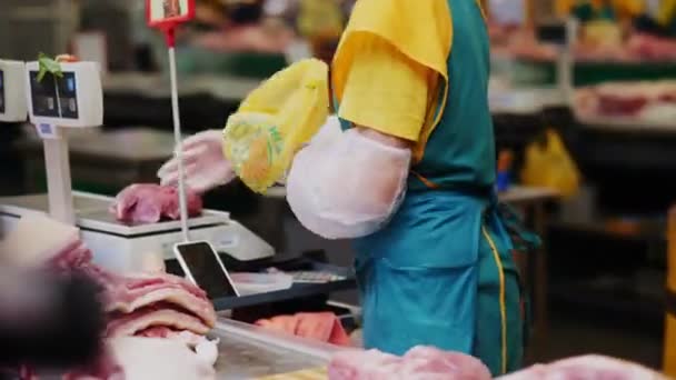 Vendedor em avental verde coloca carne fresca no saco no balcão — Vídeo de Stock