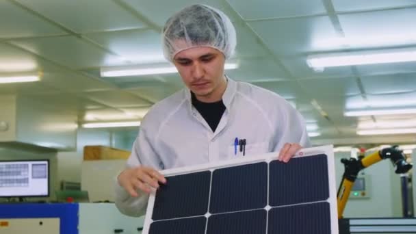 Empleado en bata comprueba panel solar con células en taller — Vídeo de stock