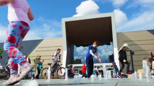Дети играют среди прыгающих струй фонтана возле торгового центра — стоковое видео