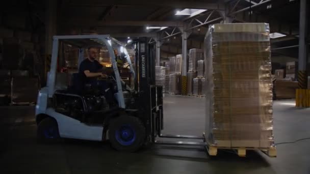 Werknemer drijft karton verpakt met folie langs magazijn — Stockvideo