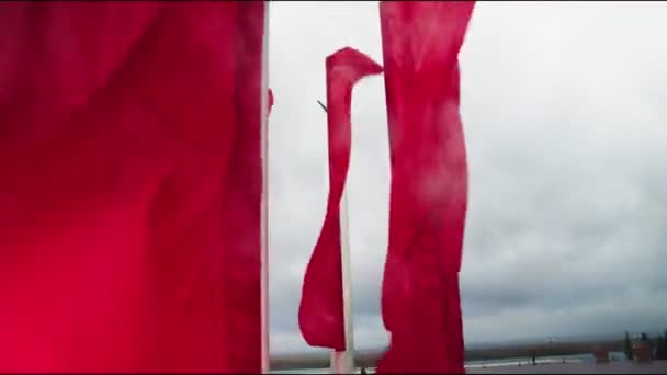 Röda flaggor våg i vinden mot monument under grå himmel — Stockvideo