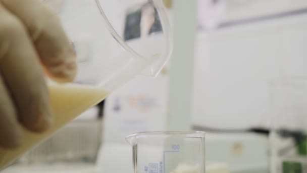 Γυναίκα ρίχνει γάλα σε ποτήρι ζέσεως με κλίμακα μέτρησης στο τραπέζι — Αρχείο Βίντεο