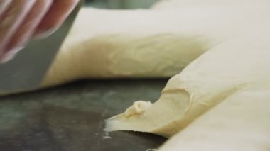 İşçi, masa üzerindeki hamur mayasını kesmek için metal levha kullanıyor.
