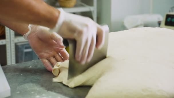 Человек использует металлический лист, чтобы разрезать сырое тесто с ножом на столе — стоковое видео