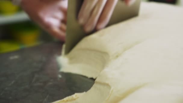 Сотрудник разрезает кучу теста на металлическом столе в пекарне крупным планом — стоковое видео