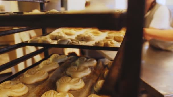 Baker puts tray with heart shaped buns to metal rack in shop — Stock Video