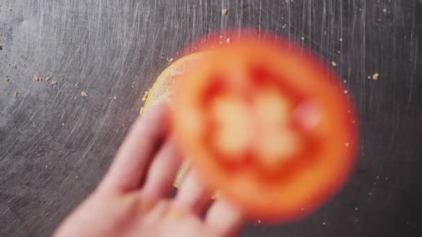 Frau wirft Tomatenscheibe auf Hamburgerbrötchen auf Metalltisch — Stockvideo