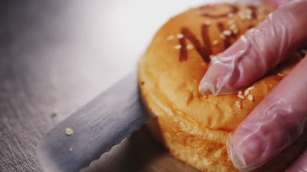 Εργάτης κόβει ψωμάκι χάμπουργκερ με σουσάμι σε μεταλλικό τραπέζι — Αρχείο Βίντεο