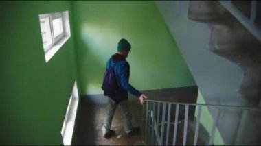 Gözlüklü adam merdivenlerden aşağı koşup yeşil duvarı geçiyor.