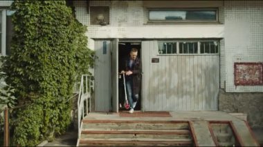 Adam binadan çıkıyor ve scooter sürüyor.