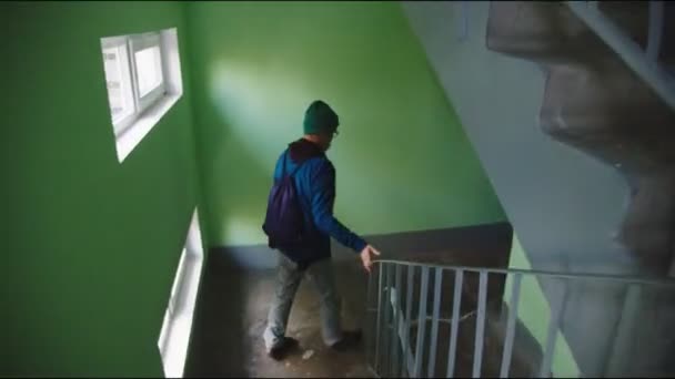 Hombre en gafas con bolsa corre escaleras más allá de la pared verde — Vídeo de stock