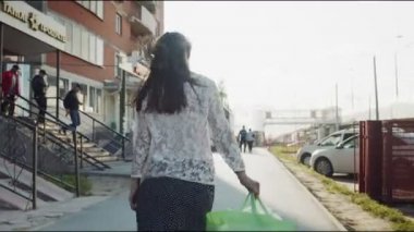 Genç bir kadın sokakta yürürken büyük yeşil bir çanta taşıyor.
