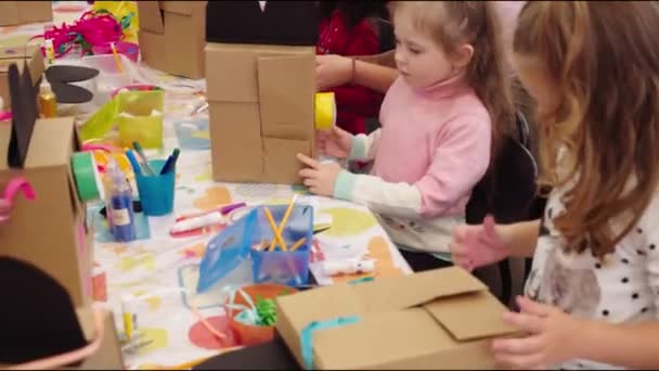 Meisjes maken ambacht met kartonnen dozen aan tafel bij kids club — Stockvideo