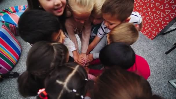 Діти й аніматор приєднуються до рук, сидячи на сірій підлозі. — стокове відео
