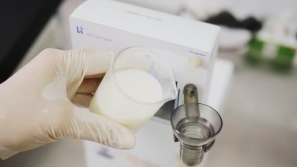 Работник наполняет стакан испытательного оборудования свежим молоком в лаборатории — стоковое видео