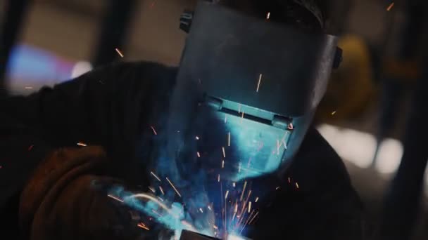 Сварщик в специальной маске соединяет металлические детали при ярких искрах — стоковое видео