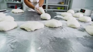 Yetenekli fırıncı atölyedeki metal masaya hamur yoğurur.