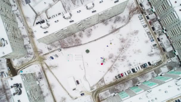 Cámara se eleva por encima de patio cubierto de nieve con parque infantil cerca de edificios — Vídeo de stock