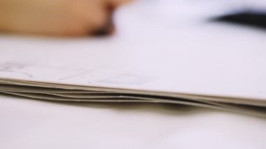 man draws line on paper sheet with pencil at table closeup