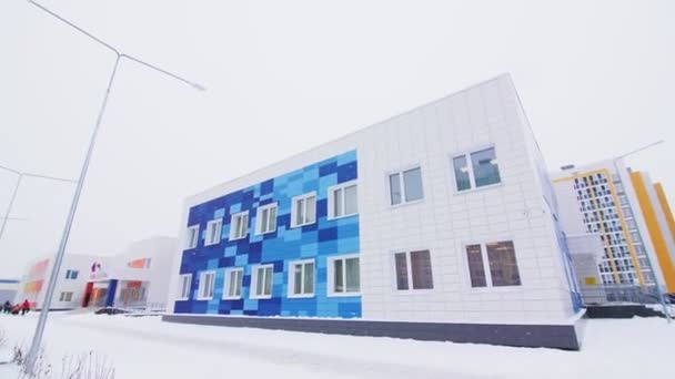 Edificio de la escuela con paredes brillantes y parque infantil en las nevadas — Vídeo de stock