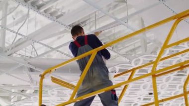 Elektrikçi alışveriş merkezinin tavanına modern lamba yerleştirdi