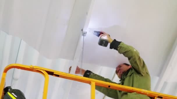 Mitarbeiter fixiert Detail an Decke mit Bohrmaschine am Bau — Stockvideo