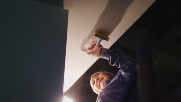 Зрелая женщина полирует потолок в темном зале — стоковое видео