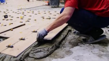 laborer in t-shirt lays tiles with hammer at construction