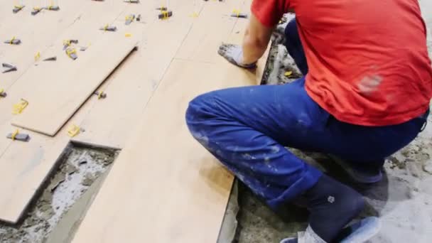 Laborer in uniform taps with hammer on tiles at construction — Stockvideo