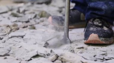 laborer in sneakers with jackhammer breaks concrete on floor