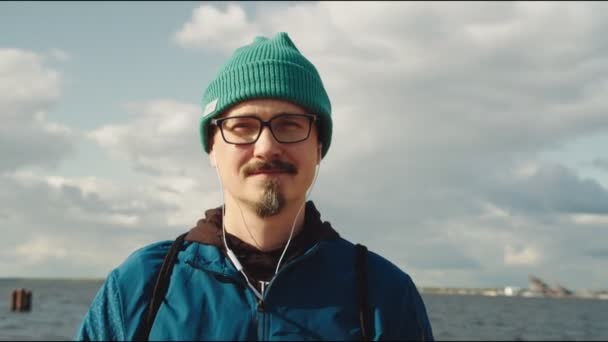 在海滨戴着眼镜和耳机的快乐的年轻人 — 图库视频影像