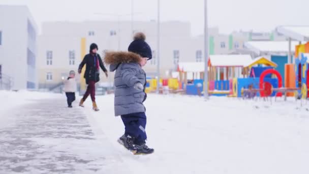 Kinder laufen auf Spielplatz im verschneiten Hof neben Kindergarten — Stockvideo