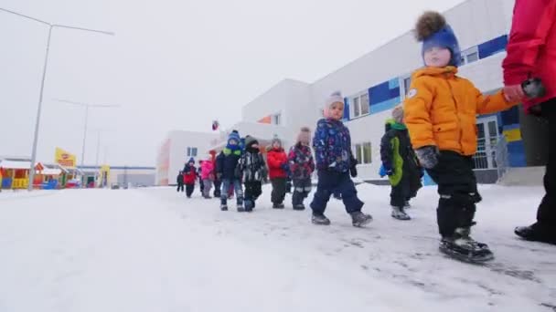 Діти з вчителем ходять по сніговому дитячому садку. — стокове відео