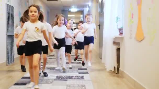 Bambini felici corrono lungo il corridoio illuminato luminoso dell'asilo — Video Stock