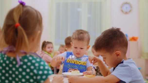 Mały chłopiec trzęsie łyżką przy kolacji w nowoczesnym przedszkolu — Wideo stockowe