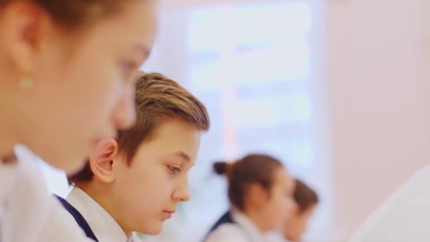 Schoolboy writes in notebook listening to teacher at desk — Stock video