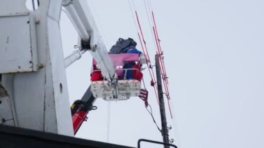 Üniformalı işçiler kamyon vinç sepetindeki elektrik hatlarını onarıyor.
