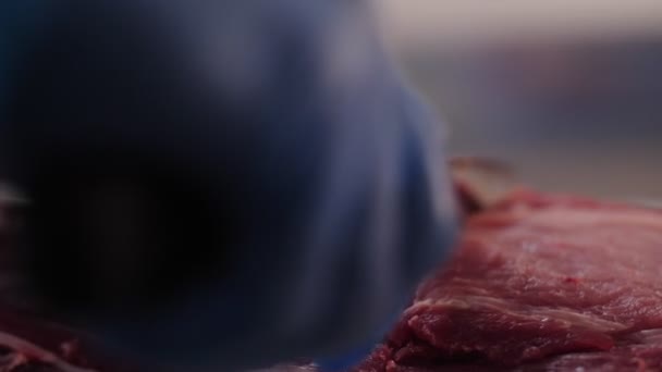 Slager in blauwe handschoenen snijdt varkensvlees met mes op tafel — Stockvideo