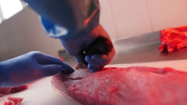 Trabajador en uniforme corta carne de cerdo fresca con cuchillo en la mesa — Vídeo de stock