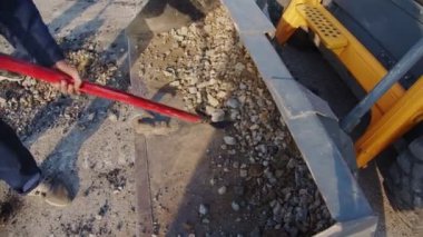 İşçiler çukurun yakınına koymak için greyder kovasından taşlar alırlar.