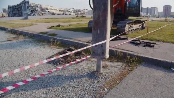 Máquina cava poço na estrada contra arena de hóquei abandonado — Vídeo de Stock