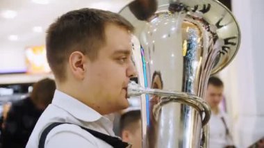 Genç adam konserde bando eşliğinde altın tuba çalıyor.