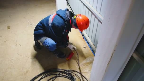 Arbetare i hatt sätter kabel i hål på golvet på stationen — Stockvideo