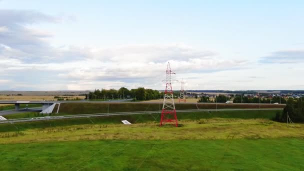Kleurrijke elektriciteitstransmissietorens in groen veld over de weg — Stockvideo