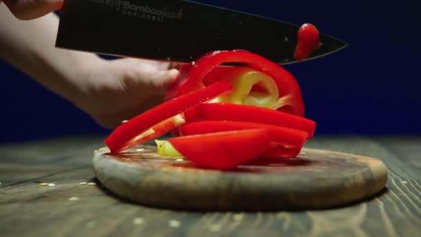 Chef snijdt rijpe rode paprika op houten plank aan tafel — Stockvideo